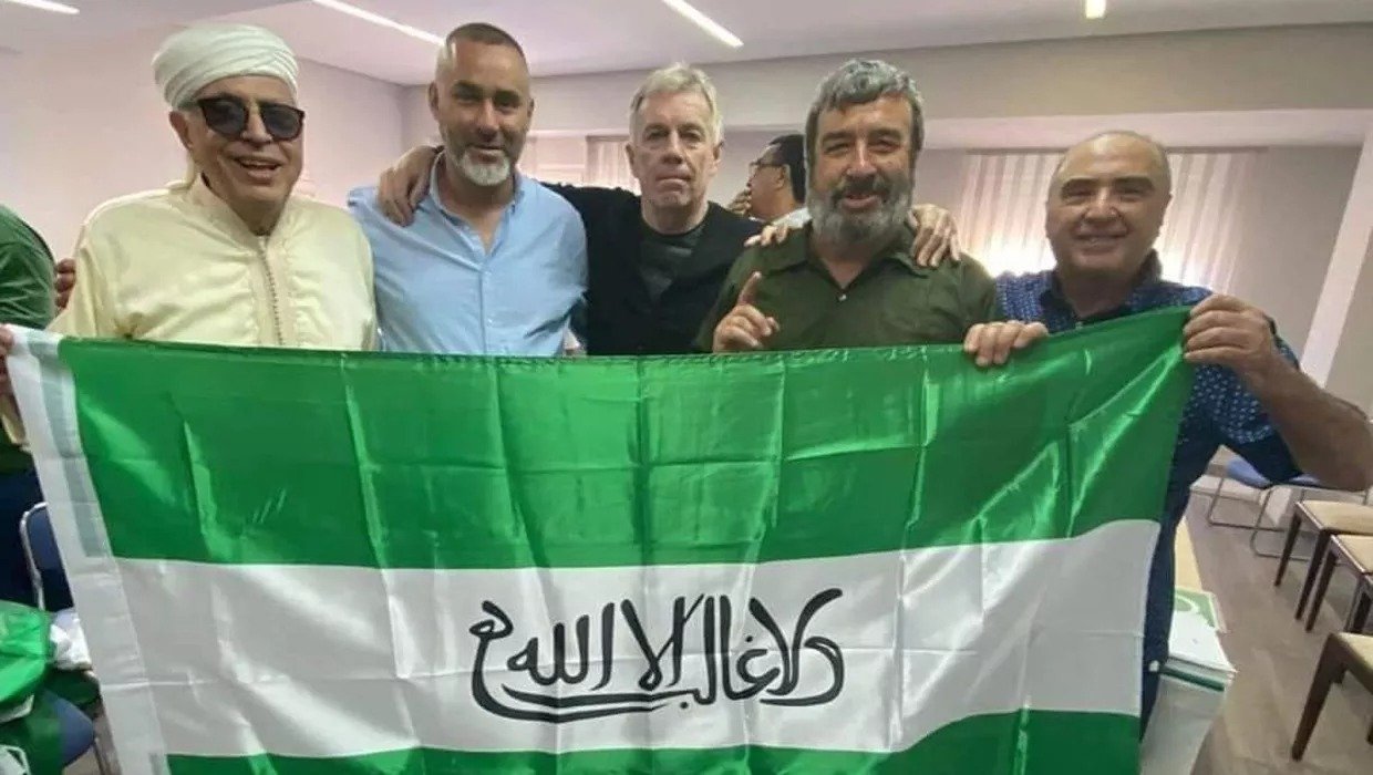 Varios integrantes del partido sosteniendo una bandera de Andalucía con unas palabras en árabe que significan ‘No hay más vencedor que Alá’